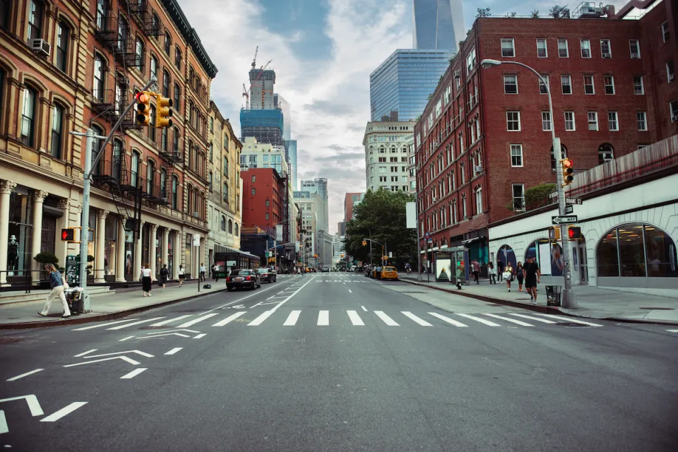 New York City street with painted bike lane and crosswalk flanked by brick buildings.